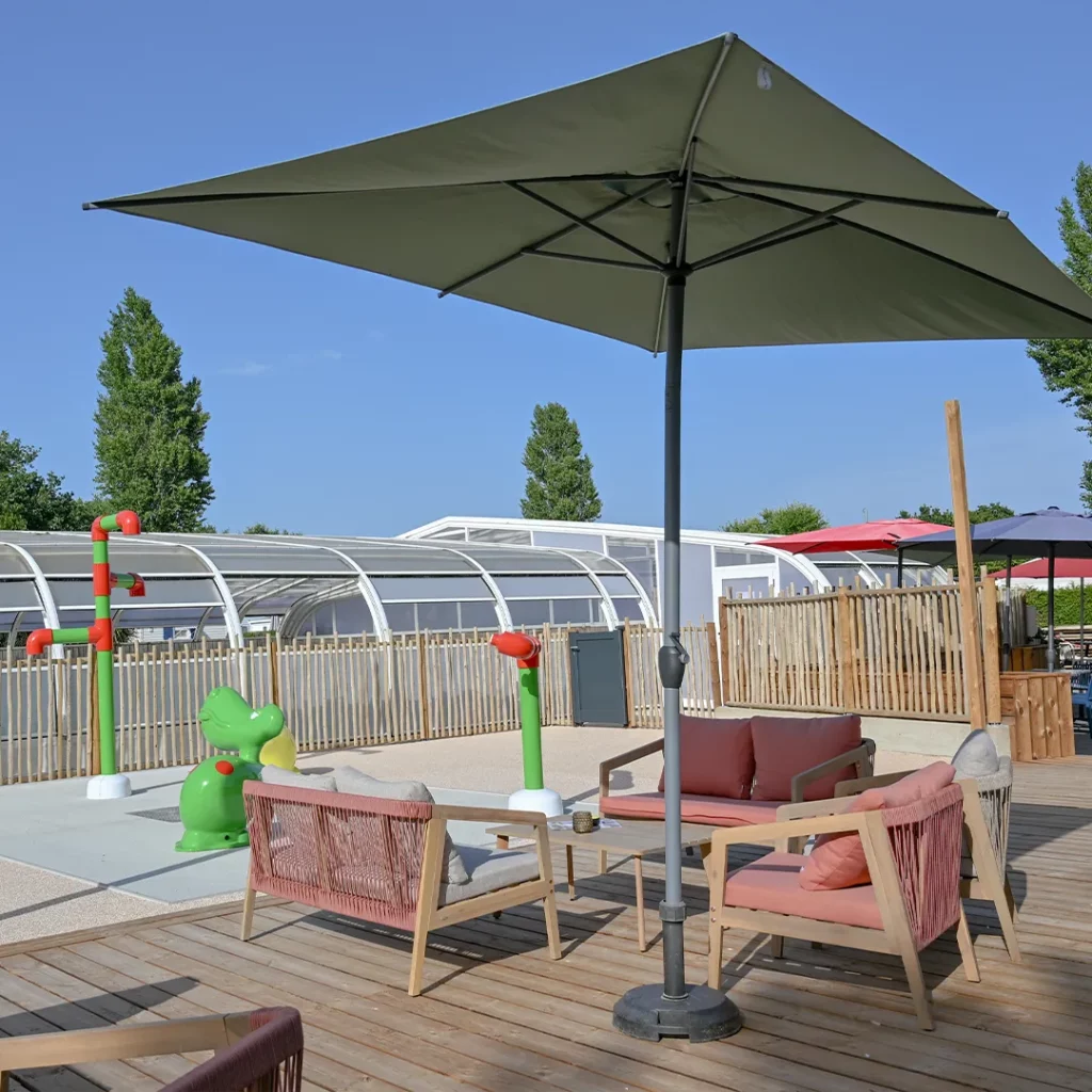 Salon de jardin sous grand parasol face aux jeux aquatiques, en Bretagne sud