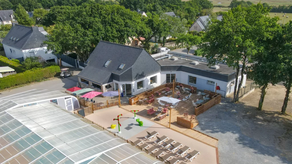 Bâtiment d'accueil, terrasse et dôme de la piscine vus du ciel, au cœur de la verdure
