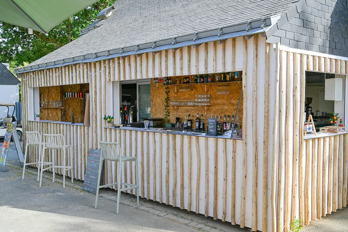 Façade en bois du snack-bar et tabourets hauts au camping Domaine du Morbihan